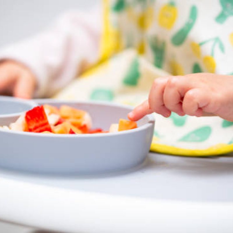 Macro Close up of Baby Hand with a Piece of Fruits Sitting in Child's Chair Kid Eating Healthy Food